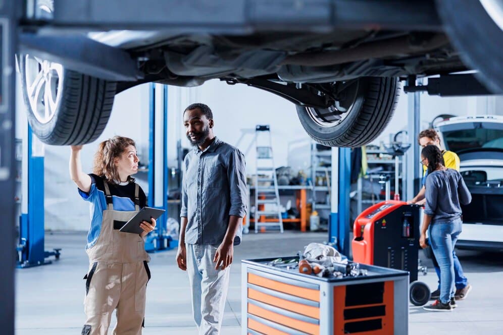 A female technician and man observing a car in an auto repair shop