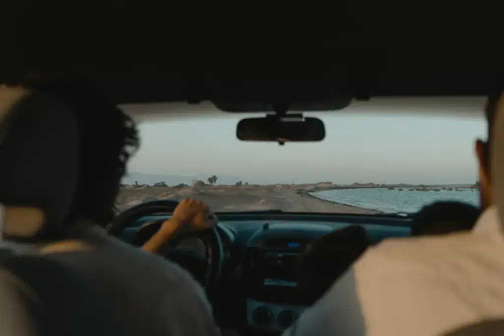 The inside of a car with people driving on the beach.