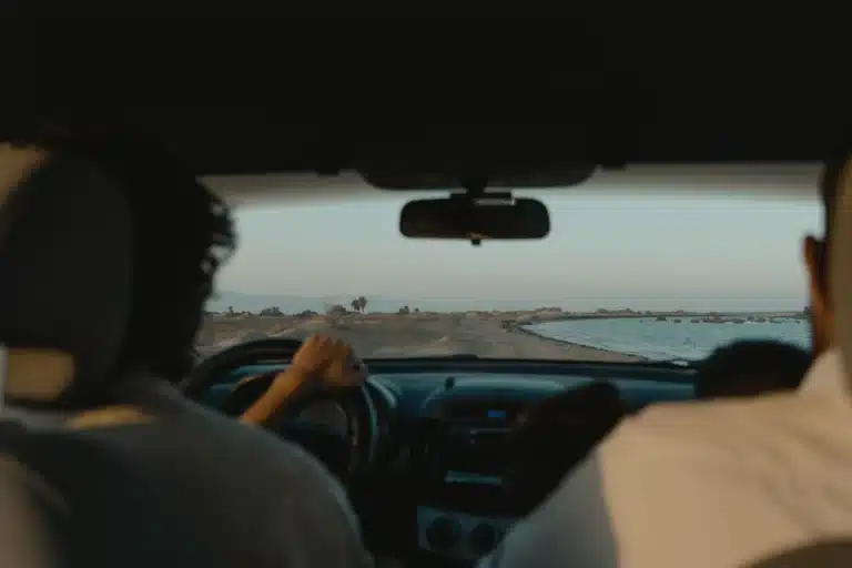 The inside of a car with people driving on the beach.